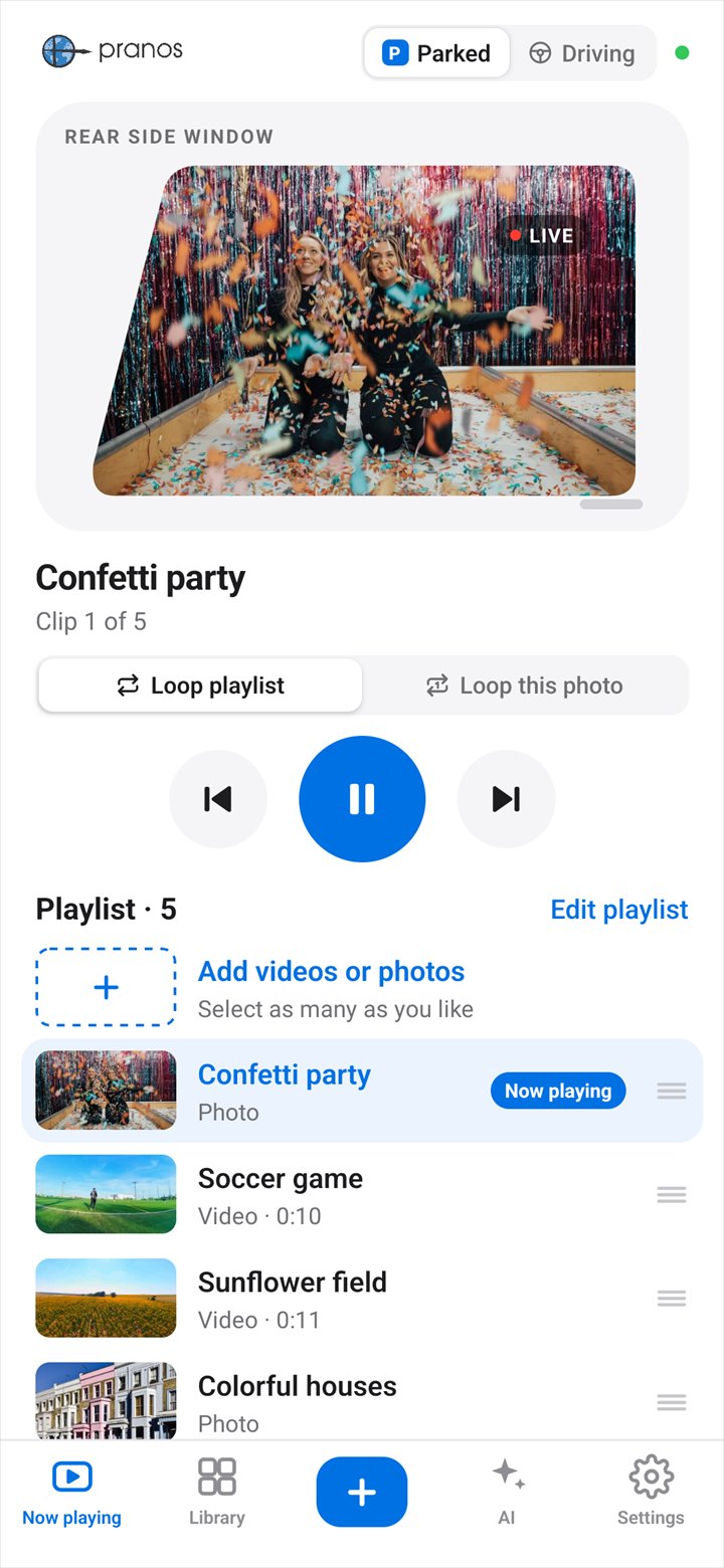 The Pranos app’s Now playing screen on a rear side window: a confetti party photo plays, with the play controls and the playlist below: a soccer game, a sunflower field, colorful houses and a hot air balloon