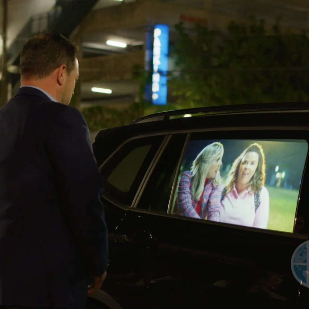 HoloGlass rear side door window display playing a video on a parked SUV at night, with a man watching