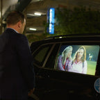 HoloGlass rear side door window display playing a video on a parked SUV at night, with a man watching